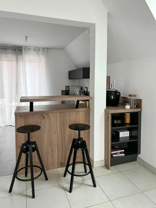 Cuisine ouverte avec comptoir bar en bois façon noyer, plan de travail surélevé, deux tabourets de bar réglables à vis style industriel, pieds métal noir
