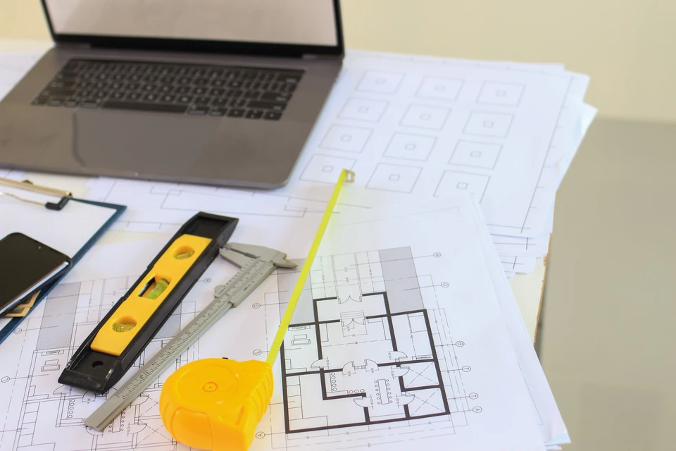 Bureau d'architecte avec plans techniques étalés, ordinateur portable ouvert et outils de mesure professionnels