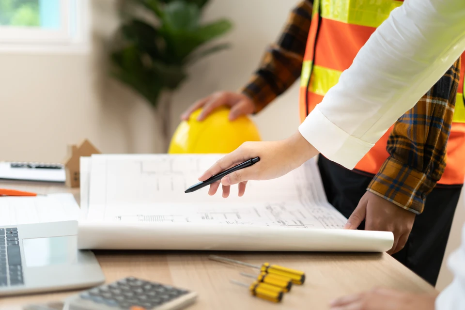 Réunion de travail en intérieur avec équipe de professionnels analysant des plans architecturaux sur table blanche